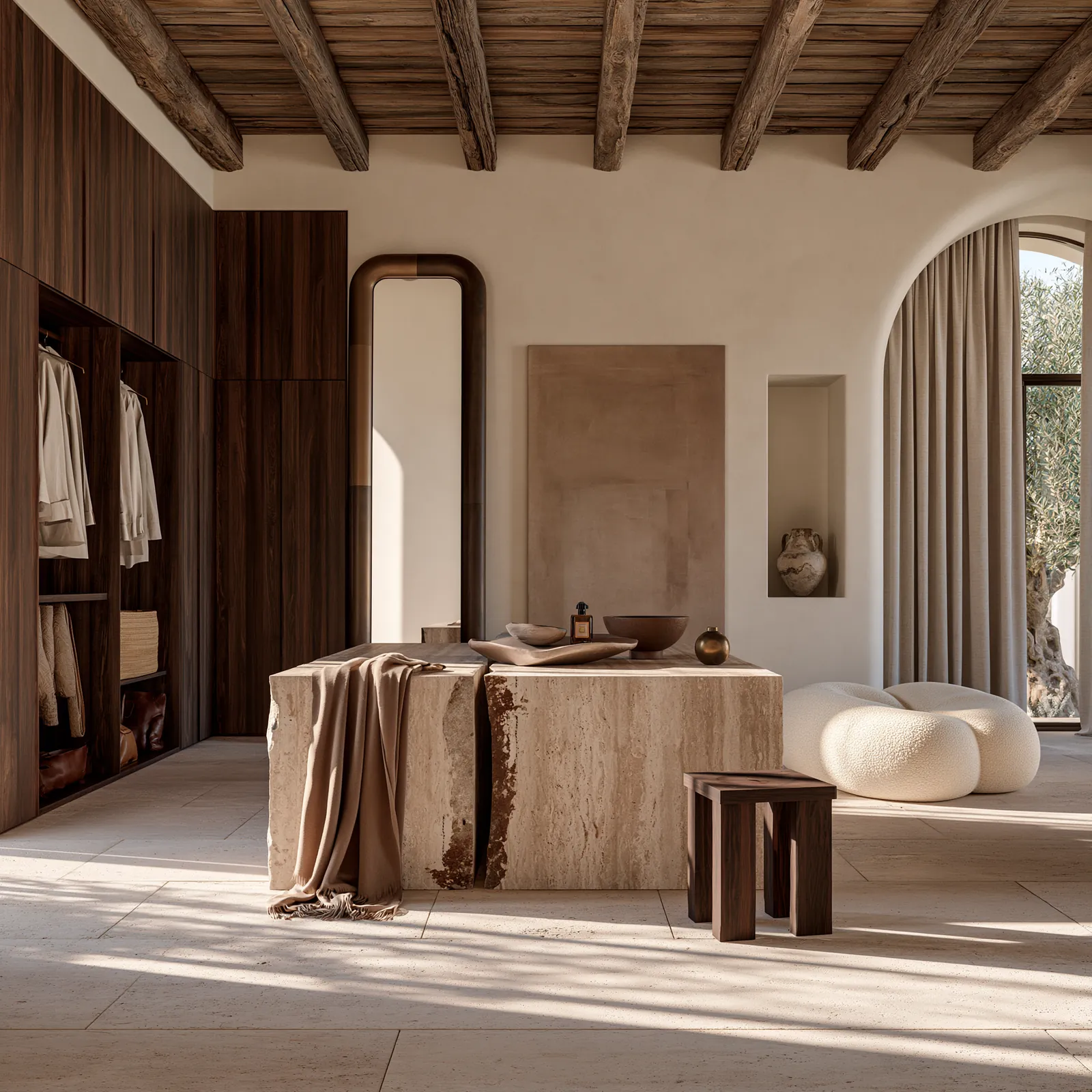 Dressing room with walnut wardrobe joinery, an open travertine island, a full-height arched mirror and a bouclé seat beside the arched window