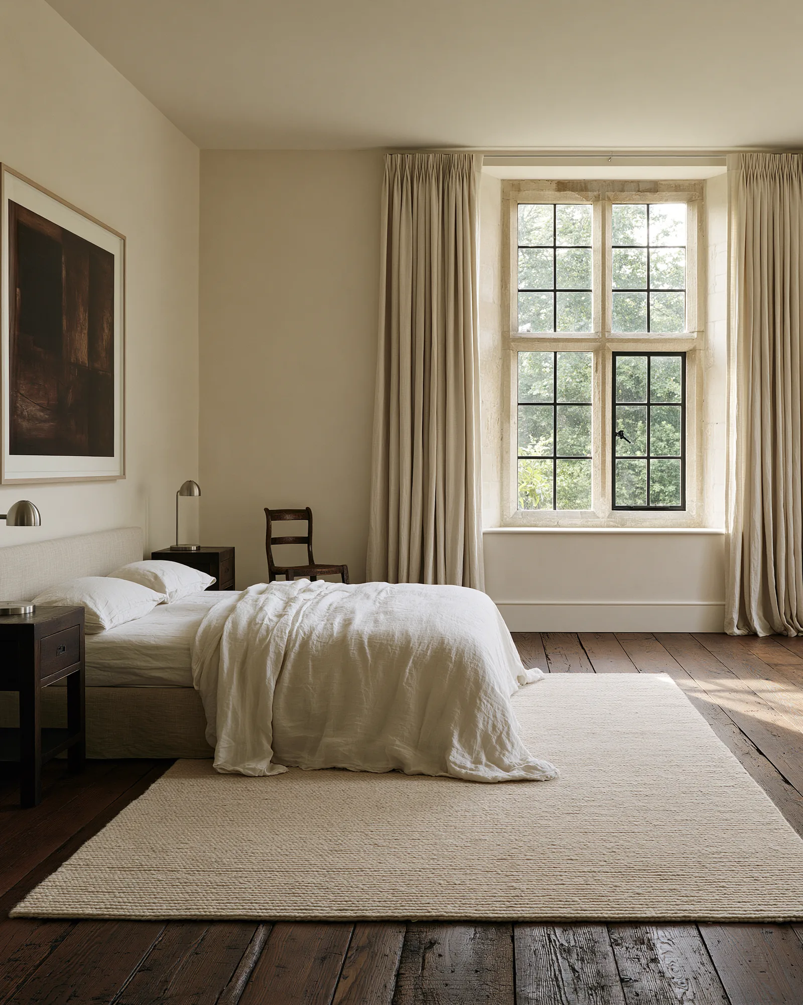Bedroom with a stone-mullioned window, pale plaster walls, linen curtains and dark timber boards