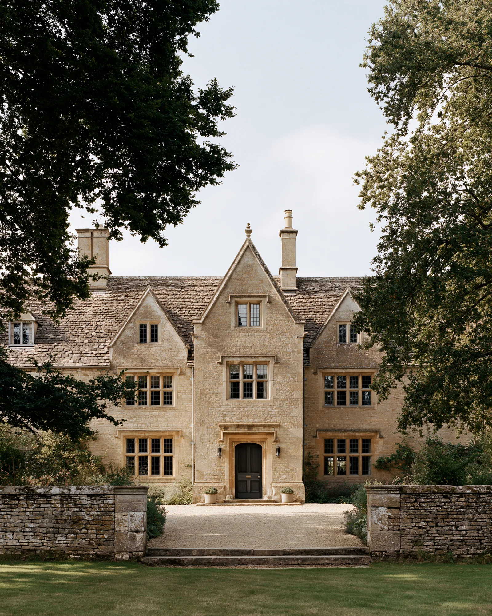 Cotswolds House — gabled Cotswolds stone facade with stone-mullioned windows, seen across the lawn
