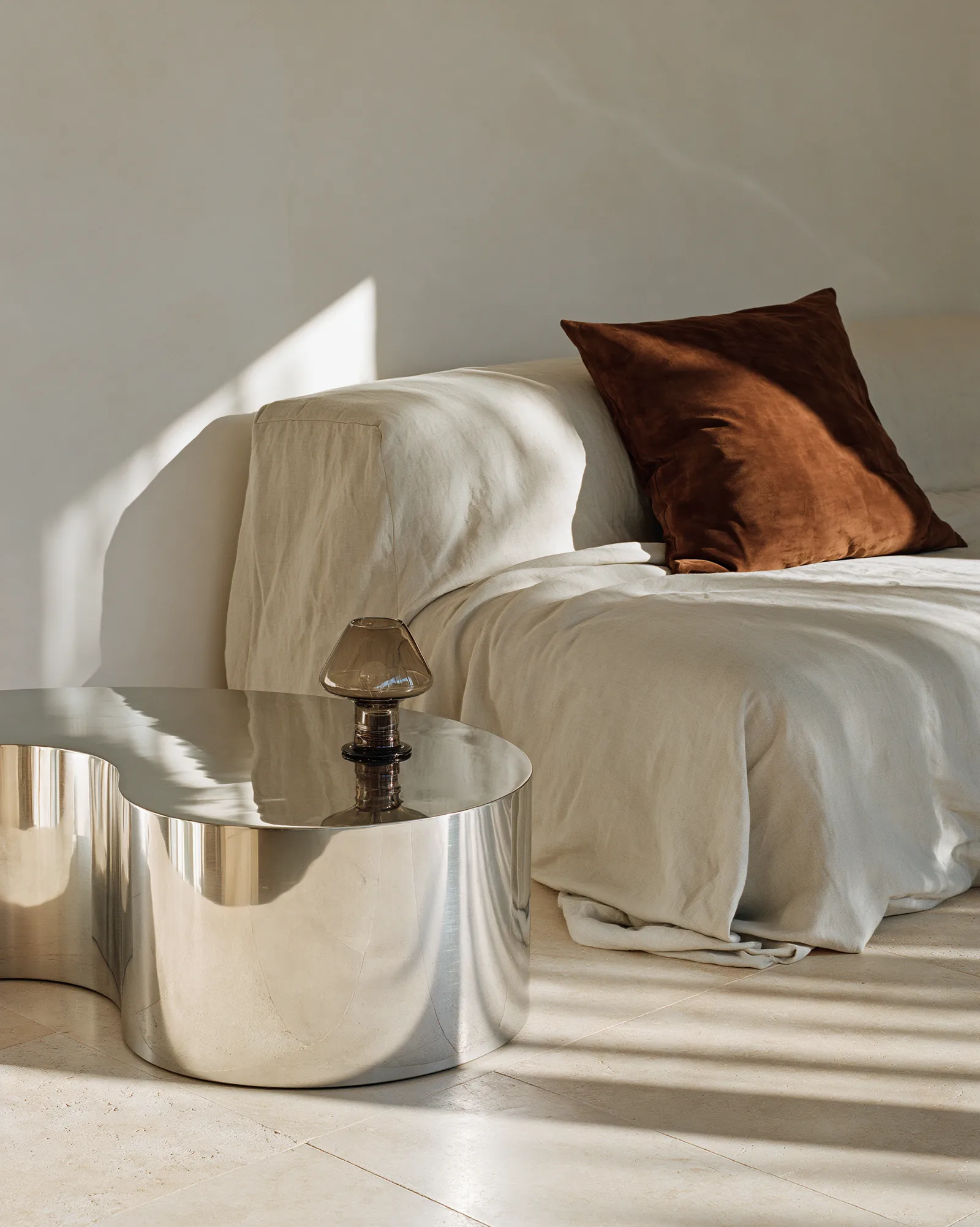 Son Vida House — oversized ivory linen seating with a rust velvet cushion and a sculptural polished steel table on pale stone, in strong Mallorcan sunlight