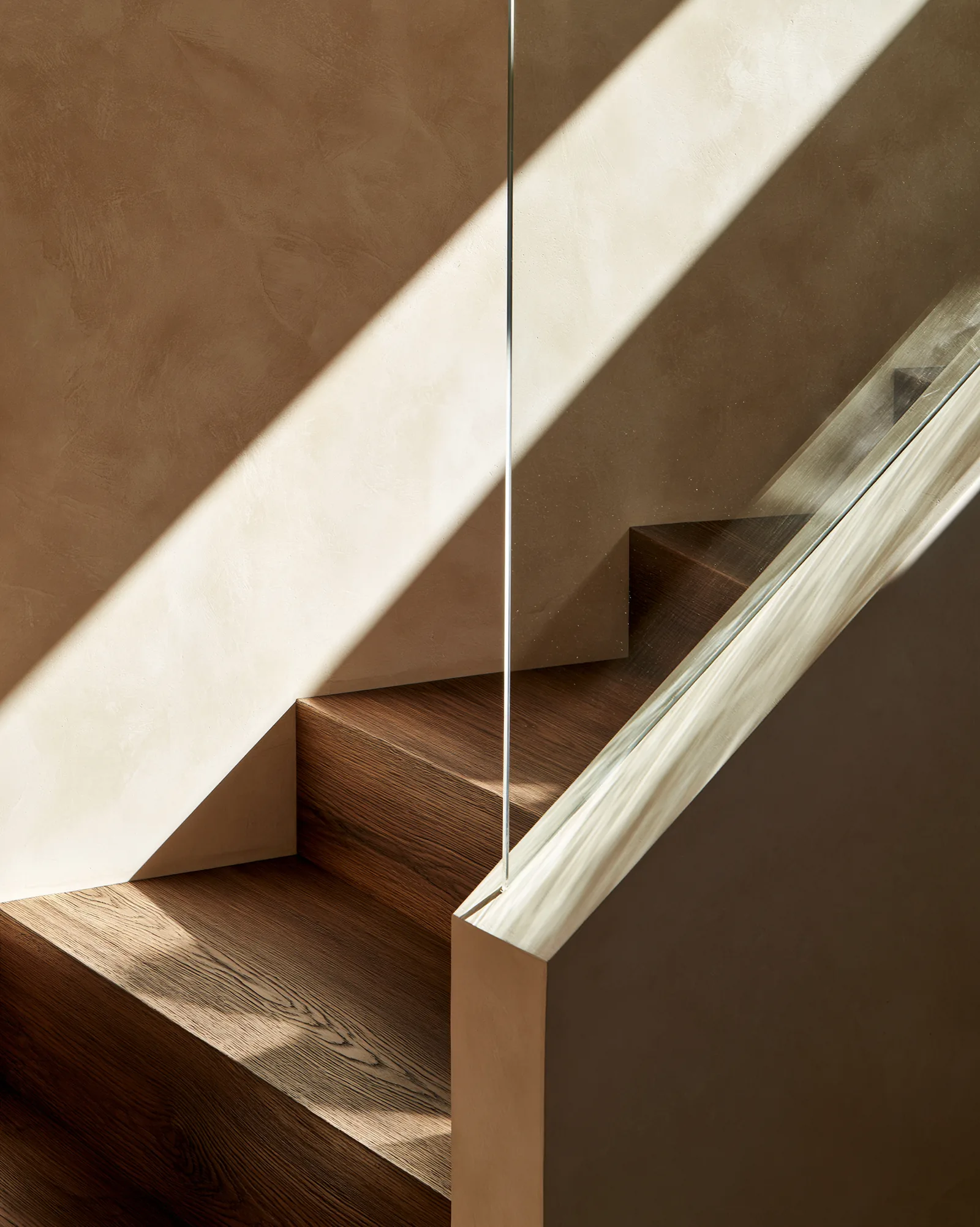 Oak treads set into warm plaster with a frameless glass balustrade