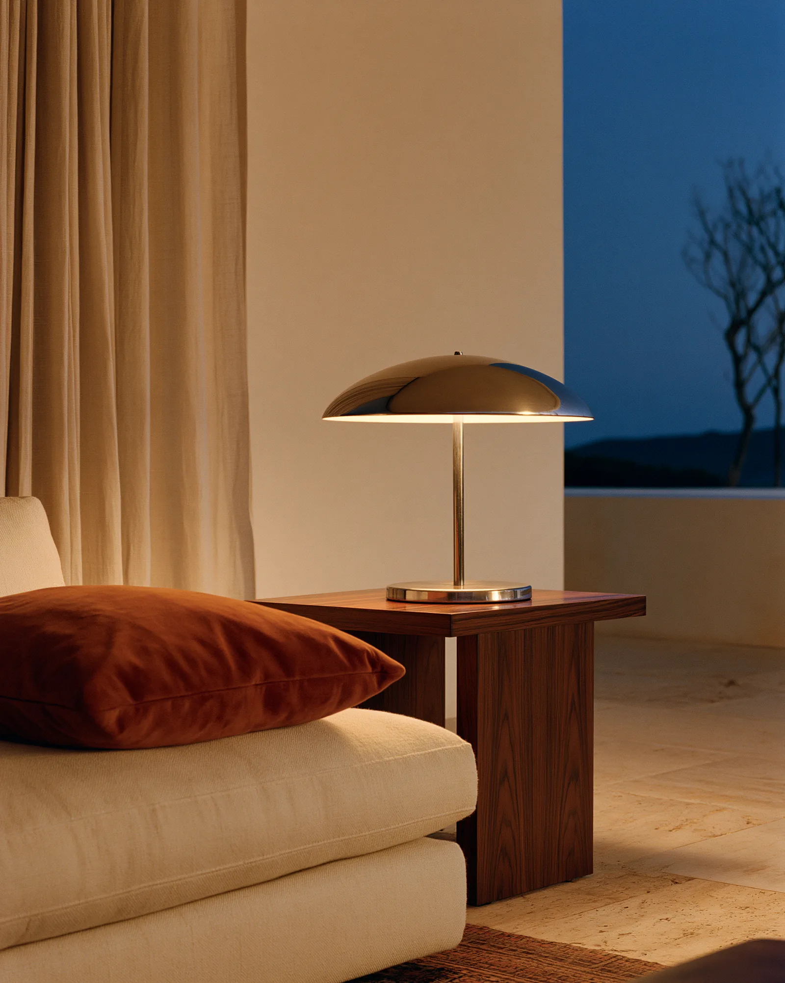 Chrome dome lamp on a walnut side table at dusk