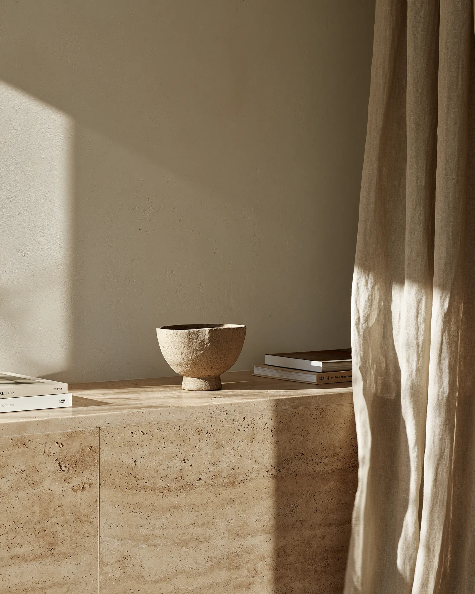 Travertine console with a raw ceramic bowl beside a linen curtain