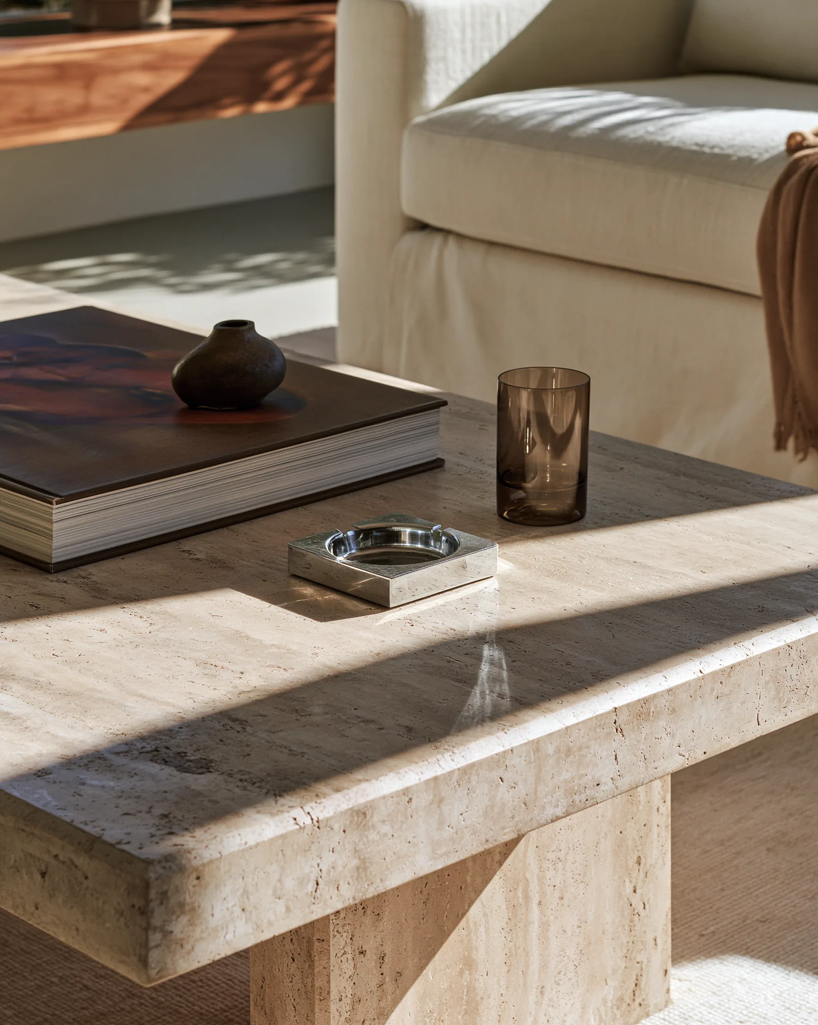 Travertine coffee table with a silver ashtray and a ceramic vessel