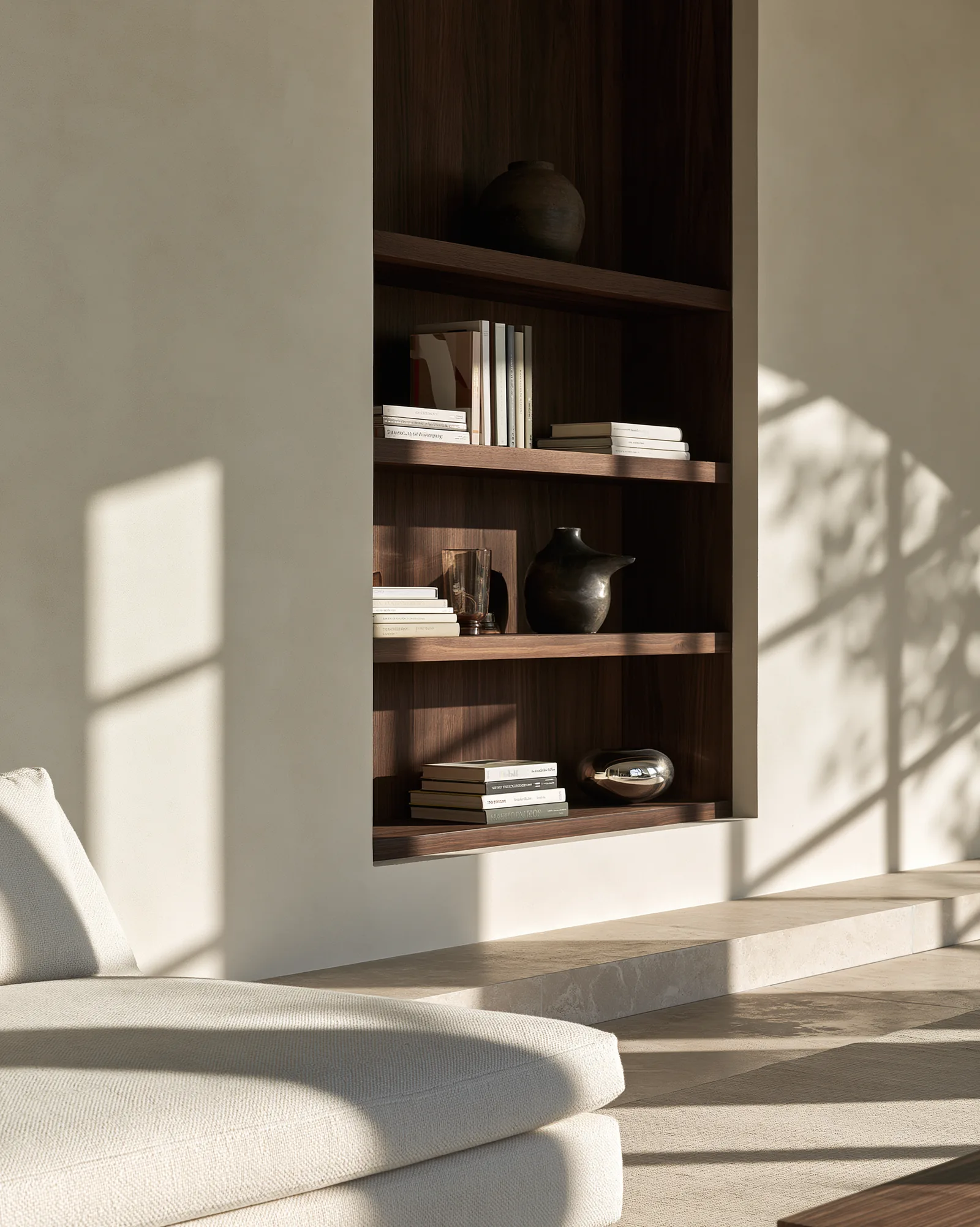 Second living space, walnut shelving recessed into a plaster wall above a stone plinth