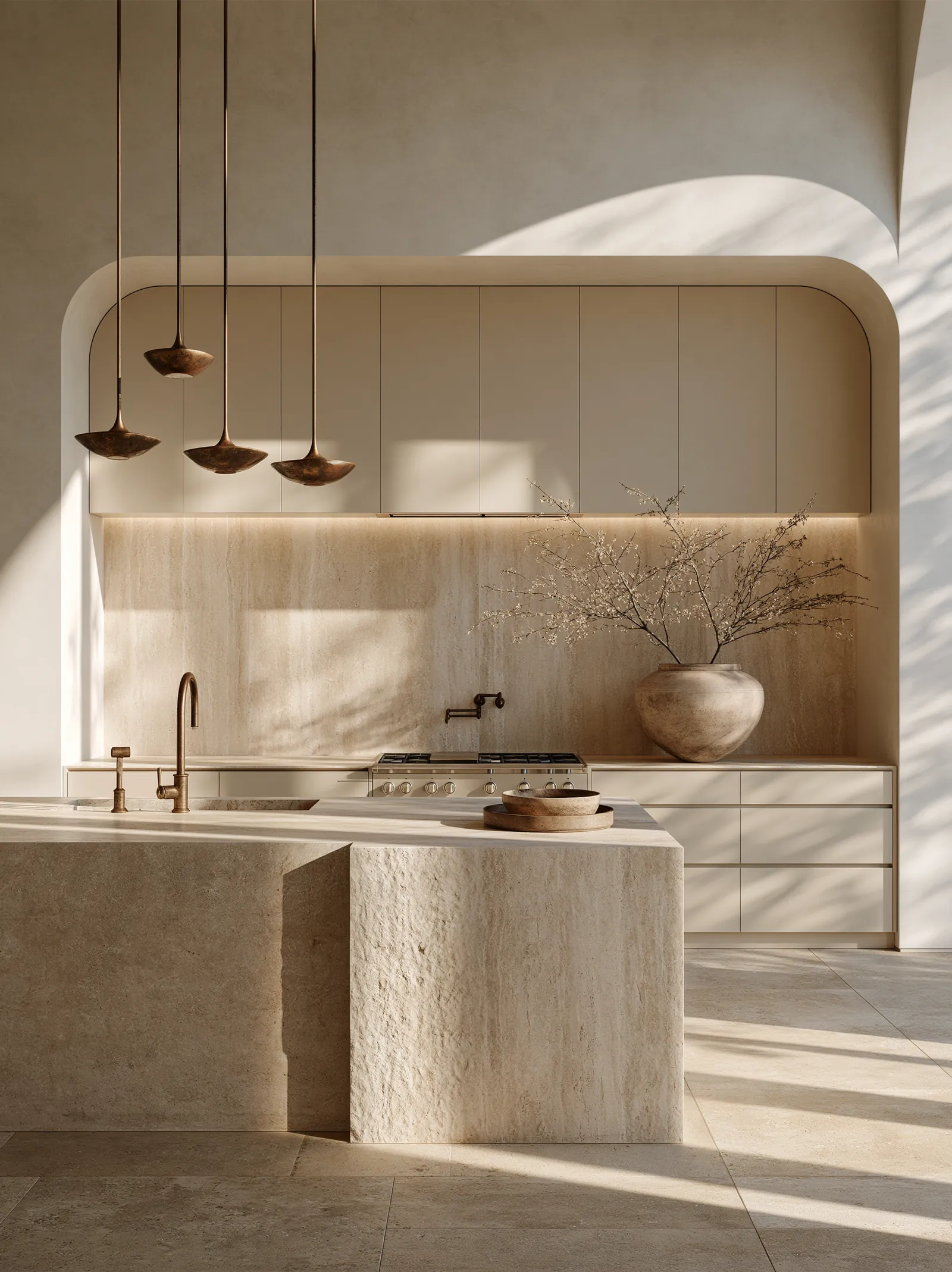 Kitchen with a travertine island and splashback under a curved plaster arch, with aged bronze pendants and a large stone vessel